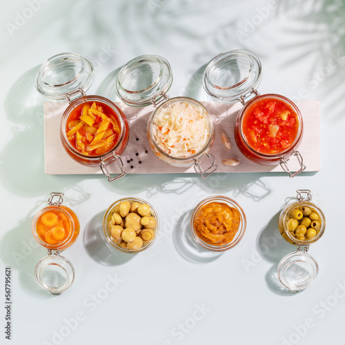 Probiotic foods. Pickled or fermented vegetables and mushrooms in glass jars on white wooden board on blue background with shadows. Home food preserving or canning. Flat lay