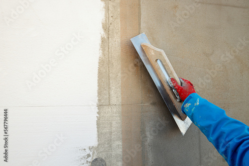 Builder plastering the wall with a spatula, fiberglass mesh, after insulating the house