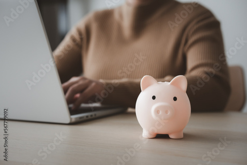 Woman working on laptop beside piggy bank for work and saving concept