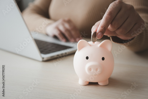 Woman working on laptop beside piggy bank for work and saving concept