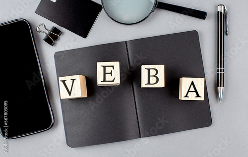 Word VEBA on wooden block on a black notebook with smartpone, credit card and magnifier photo