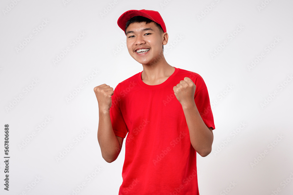 Celebration concept. Smiling young asian Delivery man in red uniform isolated on white background very happy and excited celebrating a victory with arms raised Celebration concept. Smiling young asian Delivery man in red uniform isolated on white background very happy and excited celebrating a victory with arms raised