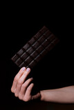 milk chocolate bar on a black background. Chocolate in a woman's hand close up