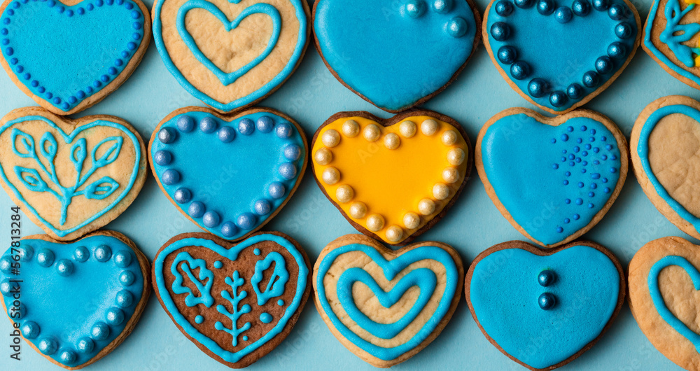 Cookies in shape of hearts decorated by yellow and blue icing and sprinkles on blue background