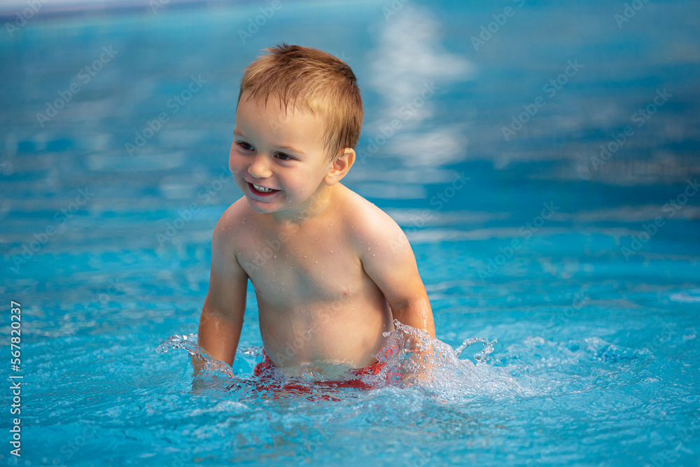 Happy little boy is playing with water in the pool.