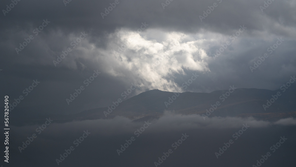 Dramatic landscape with mountain peak between fog and clouds, autumn season in mountains