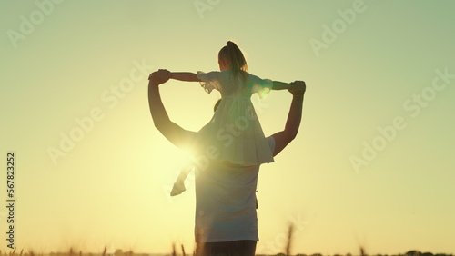 Fototapeta Naklejka Na Ścianę i Meble -  Happy child, father, runs and plays in field of wheat, little daughter on shoulders of her father, girl and dad travel across field. Kid and parents play in nature. Happy family and childhood concept
