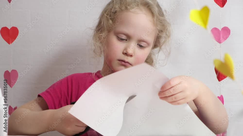 a girl of 7 years old cuts out a heart from colored paper sitting at the table a girl of 7 years old cuts out a heart from colored paper sitting at the table