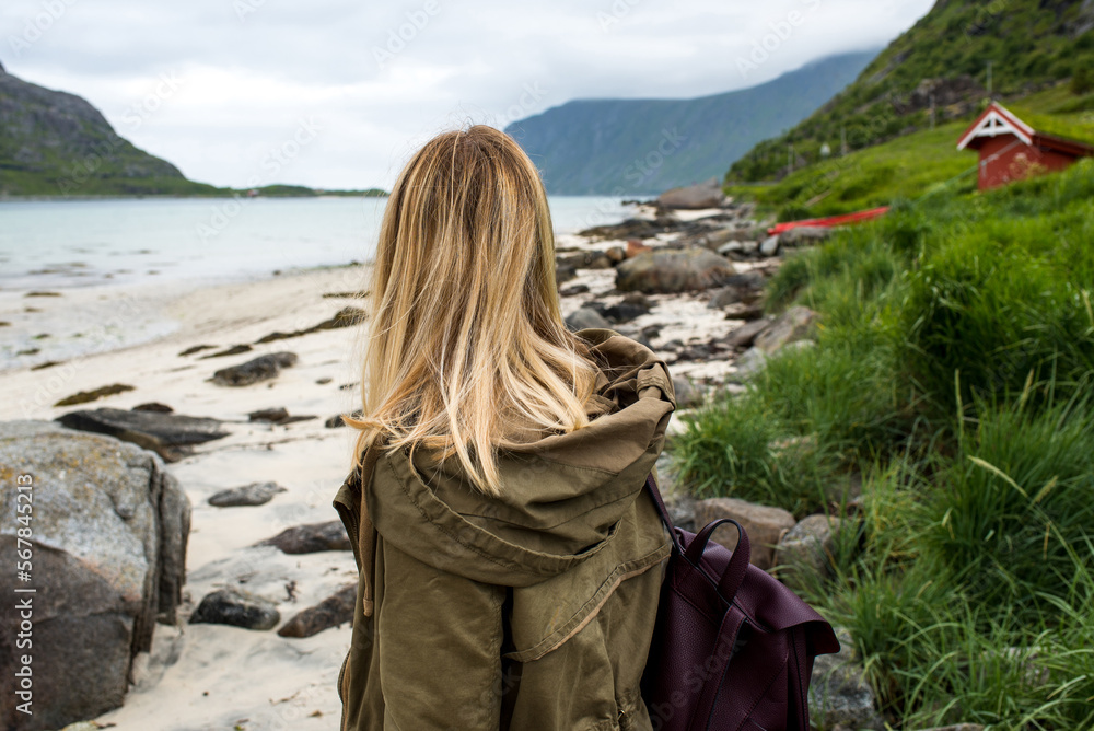 Woman with a backpack looks at the fjord. Ocean and mountain landscape. Scenic view. Travel, adventure. Sense of freedom, lifestyle. Lofoten Islands. Explore North Norway. Summer in Scandinavia Woman with a backpack looks at the fjord. Ocean and mountain landscape. Scenic view. Travel, adventure. Sense of freedom, lifestyle. Lofoten Islands. Explore North Norway. Summer in Scandinavia