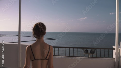A following shot of a young attractive girl in black bikini contemplates the sea from a balcony at the beach in Cadiz, Andalucia, Spain. She enjoys the sun on holidays.