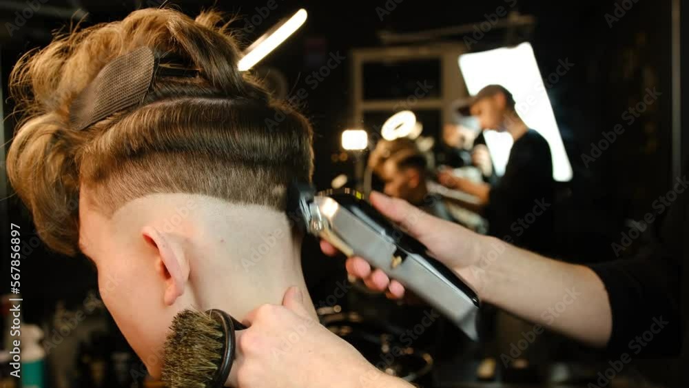 men's hairstyling and haircutting with hair clipper in a barber shop or hair salon. Hairdresser service in a modern barbershop in a dark key lightning with warm light back view. men's hairstyling and haircutting with hair clipper in a barber shop or hair salon. Hairdresser service in a modern barbershop in a dark key lightning with warm light back view.