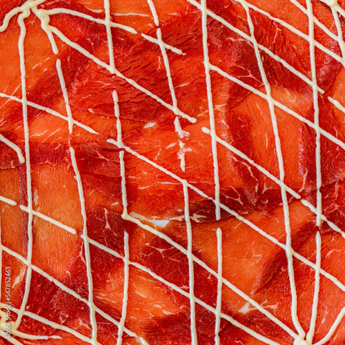 Pattern of Cipriani classic style beef carpaccio with mayonnaise sauce on a plate in close-up. The texture of an authentic Italian dish. Macro photo of thin slices of raw beef, real Italian carpaccio photo