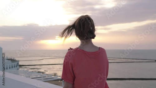 Young attractive andalucian girl contemplates the beach from a balcony in Chipiona, Cadiz, Spain, at sunset. She enjoys her holidays and smile to the camera. She wears shorts and pink shirt.