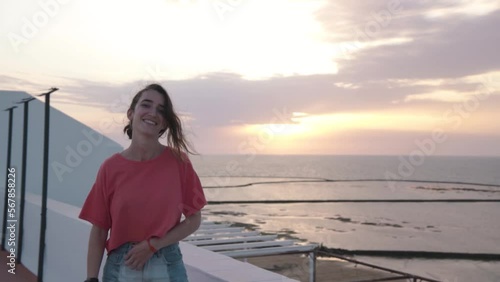 Young attractive andalucian girl contemplates the beach from a balcony in Chipiona, Cadiz, Spain, at sunset. She enjoys her holidays and smile to the camera. She wears shorts and pink shirt.