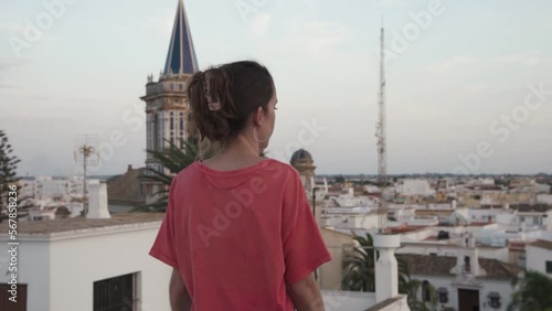 Young attractive girl contemplates a church and an andalalusian city from a balcony in Cadiz, Spain. She dances slowly. She wears shorts and a pink shirt.