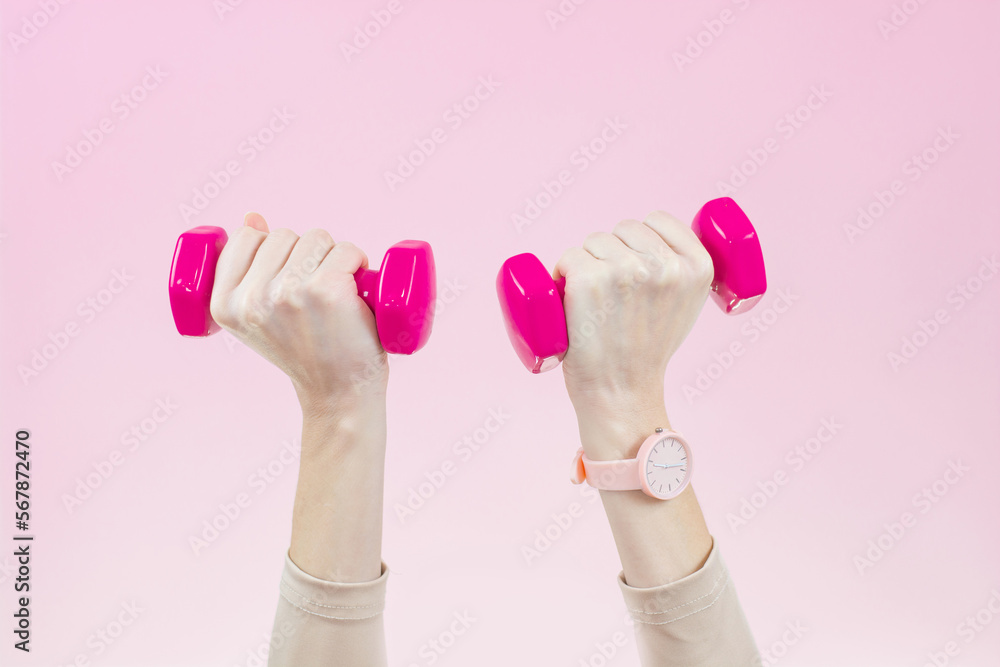 Women's hands with pink dumbbells on a pink background. Active and healthy lifestyle concept Women's hands with pink dumbbells on a pink background. Active and healthy lifestyle concept