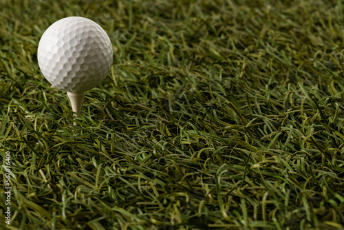 White golf ball on golf tee on grass with copy space