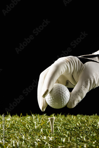 Close up of hand in white glove putting golf ball on tee on grass with copy space
