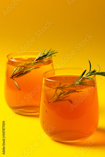 Vertical image of glasses with drinks and thyme over yellow background