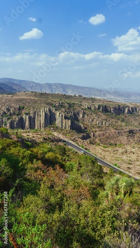 fotografia de un paisaje desertico con presencia de vegetacion desertica, de una carretera y de cuerpos rocosos como parte del paisaje