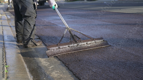 Close up of worker's feet and tool smoothing out fresh slurry seal  