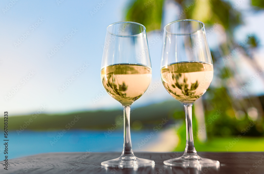Pair of wine glasses on a tropical beach bar. Romantic summer vacation sea side holiday concept.