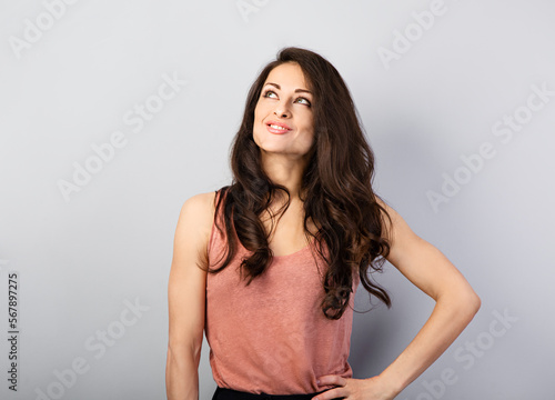 Beautiful thinking makeup toothy smiling woman with long brown healthy hair style looking up. Health care concept. Closeup portrait on blue background