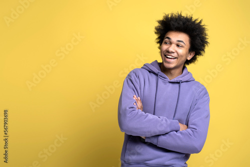 Portrait of smiling African American man with arms crossed isolated on yellow background, copy space. Happy fashion model wearing stylish casual clothes posing for photo looking away, studio shot © Maria Vitkovska