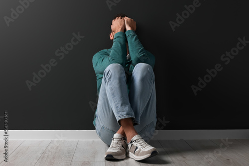 Upset man sitting on floor near black wall