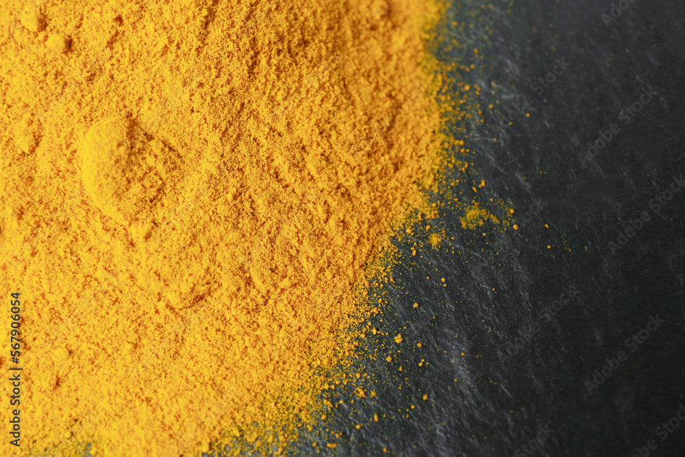 Turmeric powder on black textured table, closeup Turmeric powder on black textured table, closeup