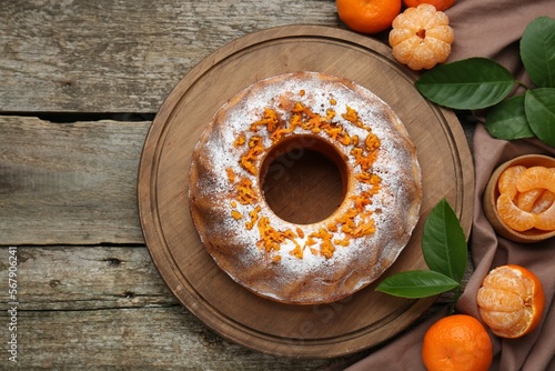 Homemade yogurt cake with tangerines, powdered sugar and green leaves on wooden table, flat lay