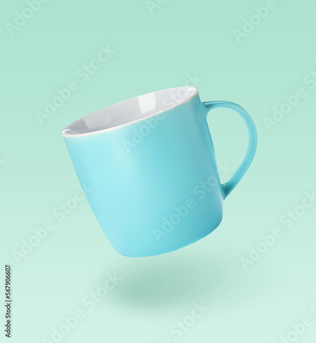 Fényképezés One empty ceramic cup falling on light turquoise background