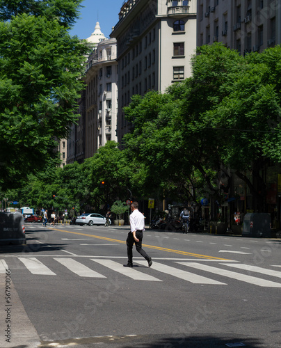 Hombre atravesanddo la calle en buenos aires, arboles frondosos al fondo 