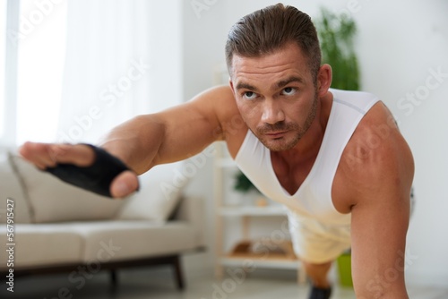 Man sports home training on the floor on a mat with dumbbells, exercises for muscle growth, pumped up man fitness trainer exercises at home, the concept of health and beauty of the body