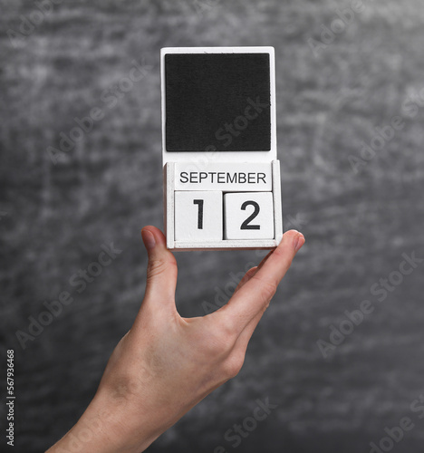 Wooden block calendar with date september 12 in female hand on background of school chalk blackboard
