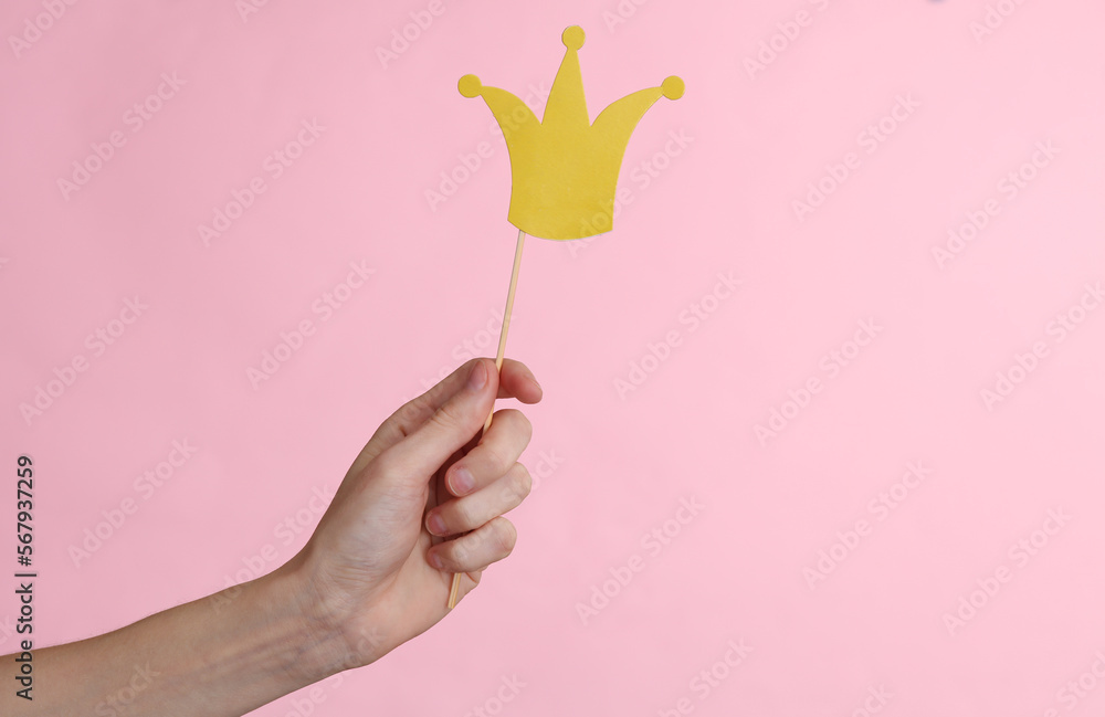 Hand holds paper cut golden crown with stick on pink background. Party concept