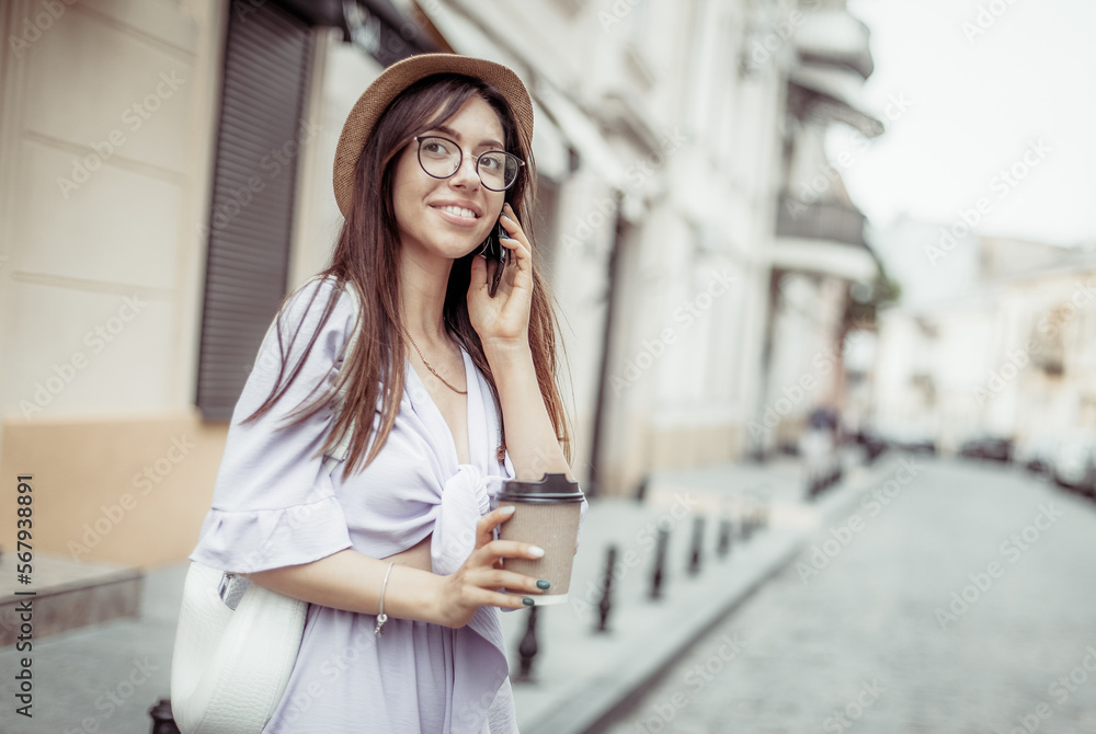 Young smiling woman talking on the phone and drinking coffee on a european street