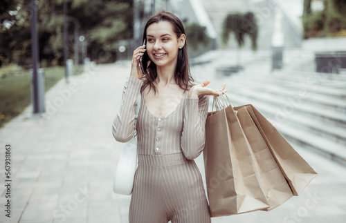 Cute smiling woman with shopping bags talking on phone outdoors. Shopping concept