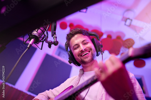Happy man, musician or guitar in neon studio, recording production or performance for radio, label or low angle concert. Guitarist, artist or singer playing strings instrument on headphones practice © N Felix/peopleimages.com