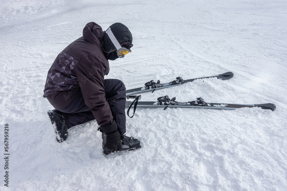 Skier getting ready to ski, attaching boots to his feet and checking equipment.