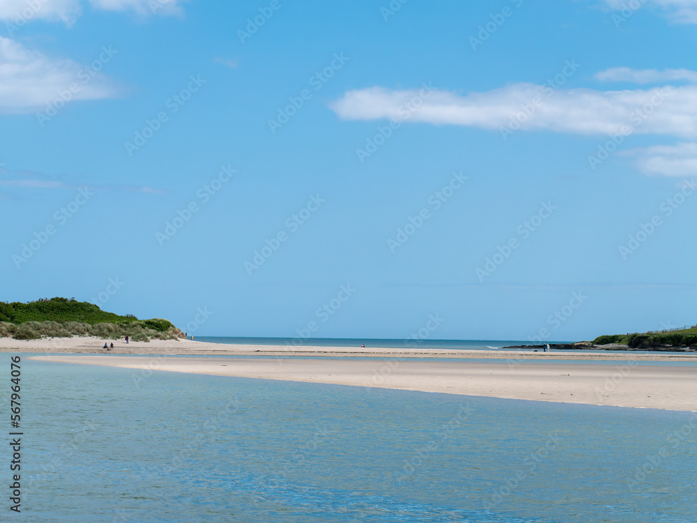 Clear sky over a beautiful sandy beach. A few people on a sandy beach. Picturesque seascape of Ireland on a summer day. A copy space. People walking on beach