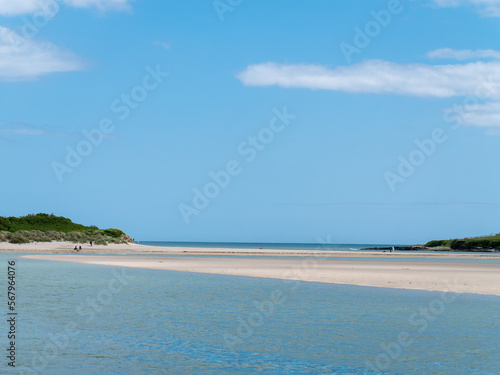 Clear sky over a beautiful sandy beach. A few people on a sandy beach. Picturesque seascape of Ireland on a summer day. A copy space. People walking on beach