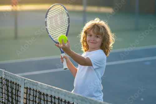 Child playing tennis on outdoor court. Child swinging racket while training on tennis. Tennis child player on tennis court. Sport concept. © Volodymyr
