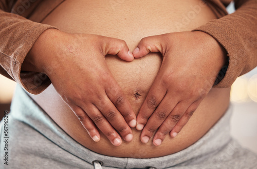 Pregnant woman, closeup of heart hands on belly and happy black mother alone in Jamaica living room. Excited future parent, holding healthy abdomen at home and loving mommy in pregnancy care