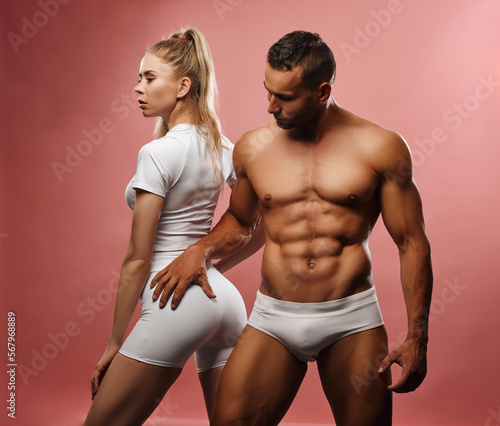 Sport couple posing on pink background. Handsome man and sexy girl like fitness motivation. Blond fitness female model with shirtless muscled male model in studio. Gym personal trainers together.