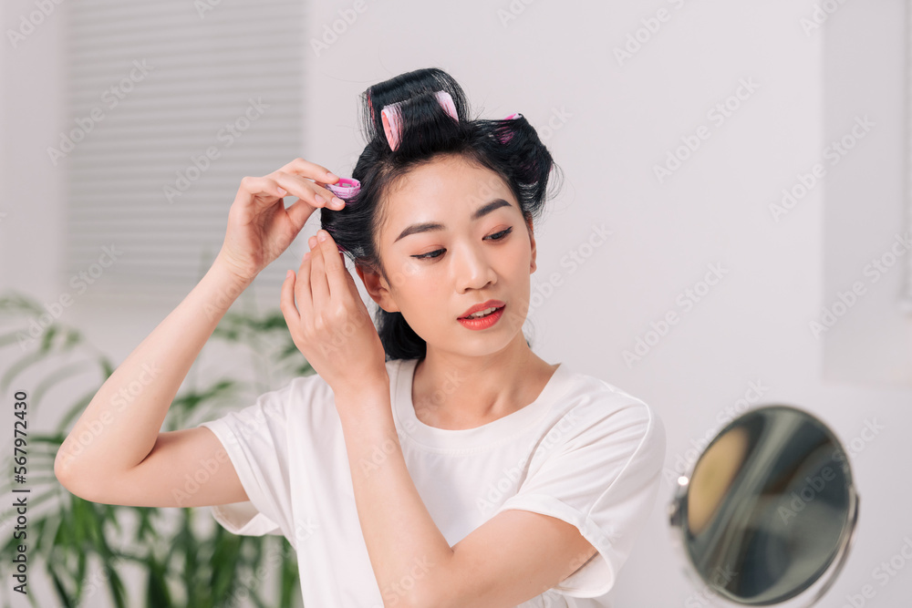 woman using hair rollers to create beautiful hairstyle on her hairdo.