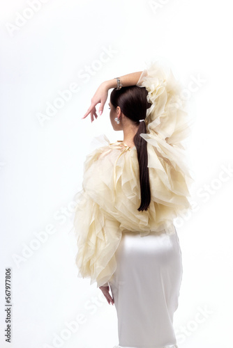 A young woman in a yellow blouse with flounces and a white silk midi skirt posing on a white background.