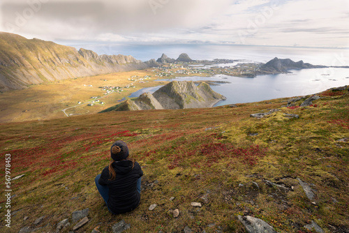 Woman Sitting On A Hill Looking At The Bay In Vaeroy, Lofoten Is photo