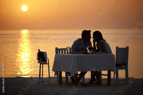 Love, ocean sunset and couple at table for romantic valentines day date at the beach in Bali in silhouette. Romance, food and wine on vacation for man and woman in loving relationship in Indonesia