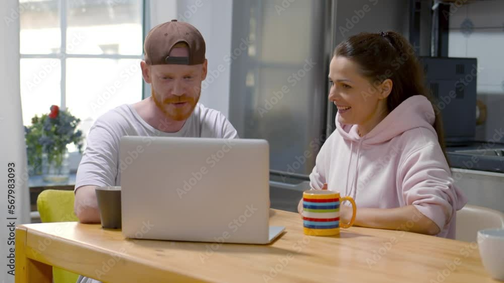 caucasian young happy couple using laptop computer having coffee in kitchen. Realtime caucasian young happy couple using laptop computer having coffee in kitchen. Realtime